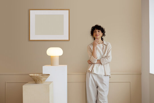 Young woman in trendy, beige room with mockup frame  