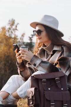 woman holding thermos coffee, texting on phone 