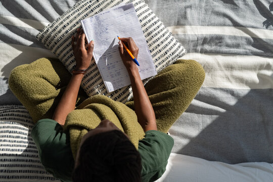 Woman writing notes in notepad on bed