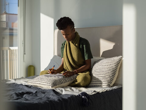 Focused female polyglot writing notes in bedroom