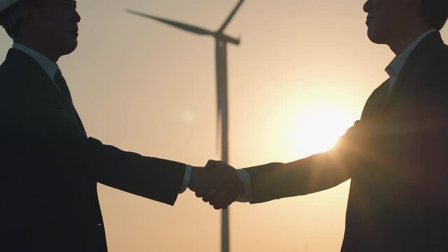 Handshake between two engineers at a wind farm at sunset, symbolizing successful negotiation and partnership in the renewable energy projects. Wind Turbine Engineering, Slow Motion