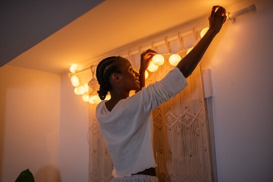 Happy black woman hanging garland on curtain rod