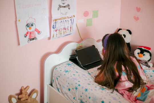 A little girl is looking at an electronic tablet lying in her bed 
