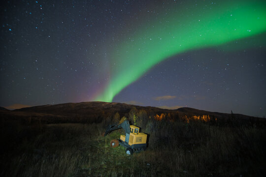 Abandoned heavy machinery excavator at night under northern lights aur