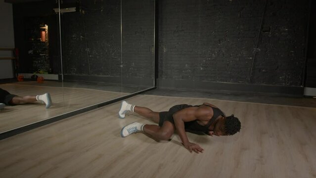 Motivated active sporty fit African man practicing advanced push up exercise with leg side crunch, strengthening upper and lower body muscles while working out in fitness club.