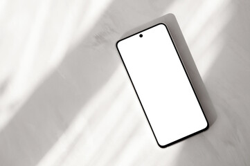 Mobile phone with blank screen mockup on neutral beige marble desk background with natural sunlight...