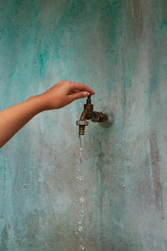 Hand opening a water tap and mint green wall woith texture