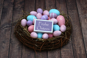 Dekoratives Osternest mit bonbonfarbenen Ostereiern, Blumen und dem Gruß Frohe Ostern.