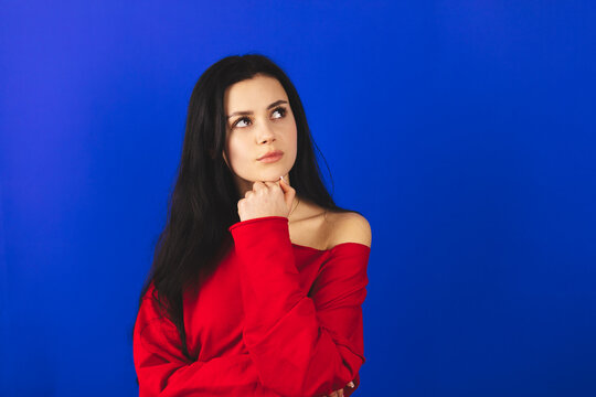 Portrait of minded brunette woman touch hand chin look at side think thoughts plan wear red long sleeves top isolated over blue color background.