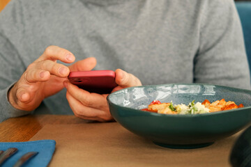 Adult Man in Grey Sweater Set at Wooden Table in Cafe, Using Smartphone. Freelancer Break. Stylish Male Enjoying Lunch and Phone Time in Cozy Restaurant, Eat Caesar Shrimps Salad. Freelancing, Leisure