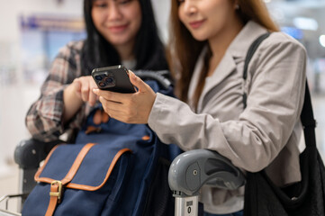 Two Asian female friends are checking their flight information and boarding time on a smartphone.