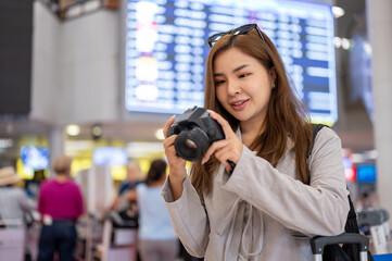 A woman is checking pictures in her camera while walking in the airport, traveling abroad.