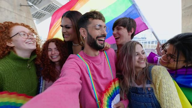 Young group of LGBT people enjoying gay pride parade festival outside. Lesbian and gay friends having fun together celebrating LGBTQI festival event together in city street.