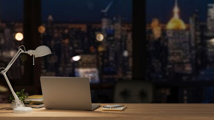 A modern office at night with a city view, featuring a laptop and accessories on a wooden desk.