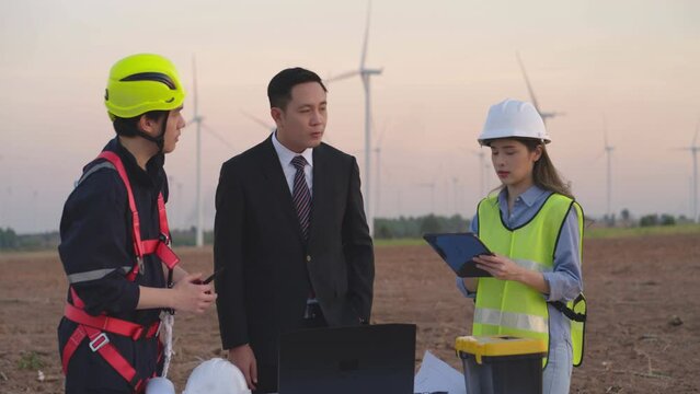 A team of engineers and maintenance technicians use laptops to assess data, inspecting wind turbines at evening, with a focus on collaboration. Renewable Energy Projects, Wind Turbine Engineering.