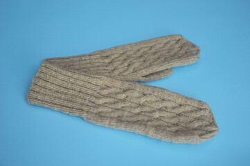 Wool knitted beige mittens with a textured pattern on a blue background. Winter accessories.