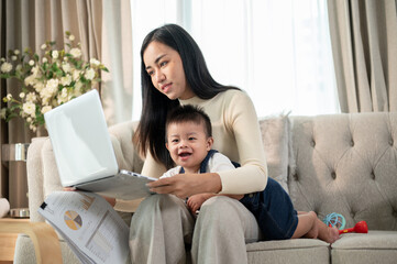 A happy Asian businesswoman mom is working from home and taking care of her naughty baby boy.