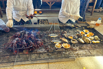 海女小屋で新鮮な伊勢海老や貝、魚を炭火焼きにする海女さん 三重県日本