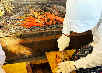 炭火焼きにした伊勢海老を海女さんが包丁で切る 三重県日本