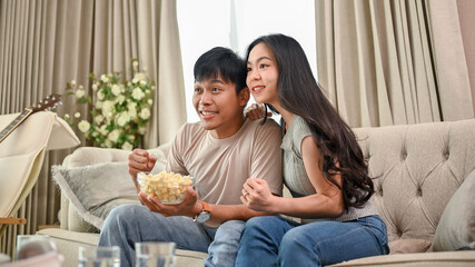 A cheerful Asian couple is watching an exciting sports match or game show together at home.