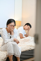 An unhappy, sad Asian wife is sitting on the bed and crying after an argument with her husband.