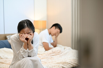 An unhappy, sad Asian wife is sitting on the bed and crying after an argument with her husband.