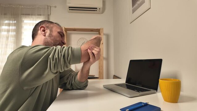 Man with elbow pain while working on a laptop.