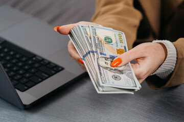 Women's hands hold a stack of money on the background of a laptop computer. The concept of financial savings, banking services, earning money on the Internet.