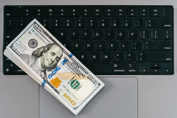 A stack of money on a laptop computer keyboard. Concept of financial savings, banking services, making money online and deposit.