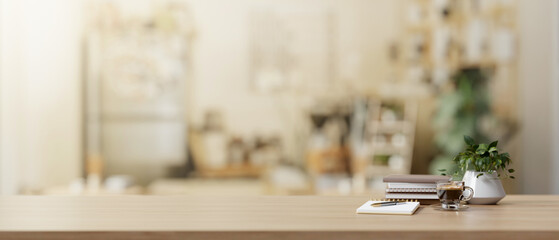 A copy space on a wooden desk features books, a coffee cup, and a potted plant in a living room.