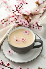 Spring twigs with flowers with a cup of hot drink, on a light wooden background.