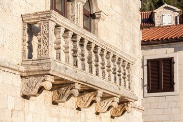 Perast, Montenegro. Detailed stone balcony with intricate balusters. Baroque influences, blending with the Mediterranean style of the region, against the backdrop of a shuttered window