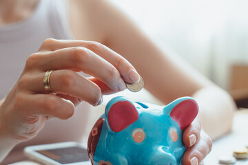 Close up young female hands putting coin in funny piggy bank.