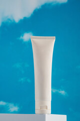 Plastic white tube for cream or lotion. Skin care or sunscreen cosmetic with stylish props on sky background 