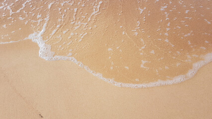 Seawater with a foamy edge rolls onto the sandy coast of yellow color