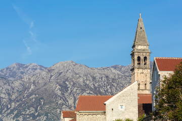 Fototapeta na wymiar Bell tower rises against a mountain backdrop in Perast, Montenegro; a red-tiled roof and stone walls highlight historical architecture typical of the Adriatic