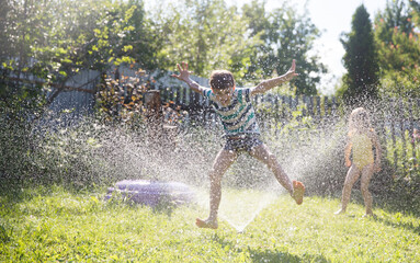 Summer holiday. Happy two kids siblings playing with garden hose and having fun with spray of water...