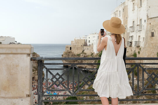 Female tourist taking photos with mobile phone at Polignano A Mare
