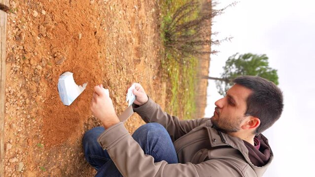 Man burying biodegradable material with seeds in a park. Vertical