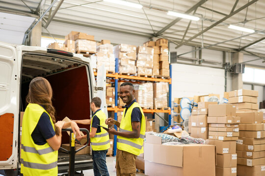 Multiracial Workers Unloading Delivery Van In Warehouse 
