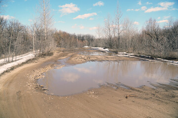 A muddy spring country road with big puddles and melting snow