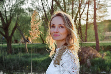 Wiosenny portret młodej ładnej uśmiechniętej kobiety, blondynka w parku, nas stawem, wśród drzew. - obrazy, fototapety, plakaty