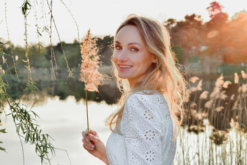 Wiosenny portret młodej ładnej uśmiechniętej kobiety, blondynka w parku, nas stawem, wśród drzew.
