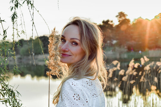 Wiosenny portret młodej ładnej uśmiechniętej kobiety, blondynka w parku, nas stawem, wśr&oacute;d drzew.