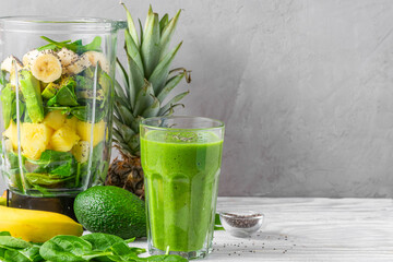 Glass of green smoothie with fresh juicy fruits, spinach, avocado, chia seeds and blender for making healthy detox drink