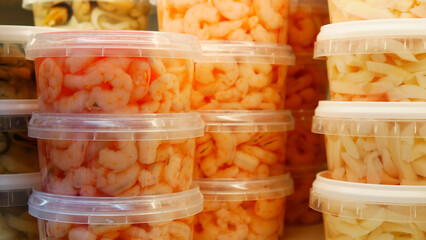 Close-up of many plastic containers of marinated shrimps and other seafood on a store shelf.