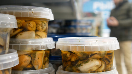 Close-up of many plastic containers with mussels in marinade and a male buyer chooses one behind them
