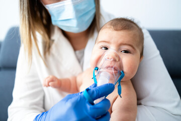Doctor pediatrician using nebulizer for baby inhalation.