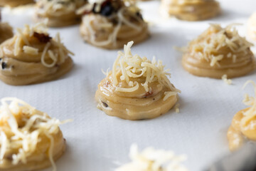 Close up of uncooked French gougères or cheese puff topped with grated cheese, while preparing to put in oven. It's a traditional pastry made with savory choux dough.