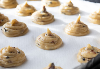 Close up of uncooked French choux pastry dough in a baking tray with chopped olives. It's a preparation step to cook a dessert base of savory choux dough bun